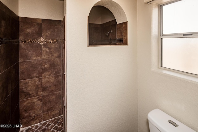 bathroom featuring toilet, a tile shower, and a textured wall