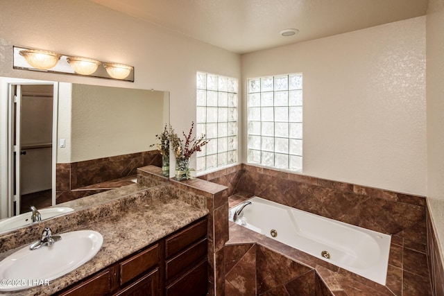 full bathroom featuring a textured wall, a jetted tub, and vanity