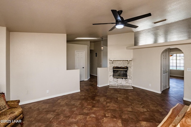 unfurnished living room with arched walkways, ceiling fan, a fireplace, visible vents, and baseboards