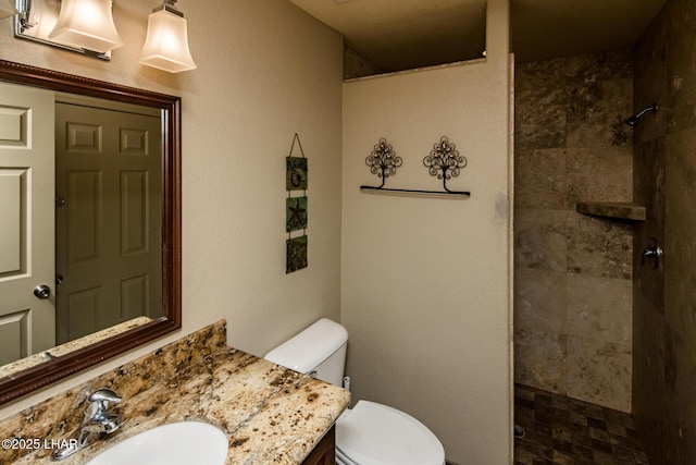 bathroom featuring a tile shower, vanity, and toilet