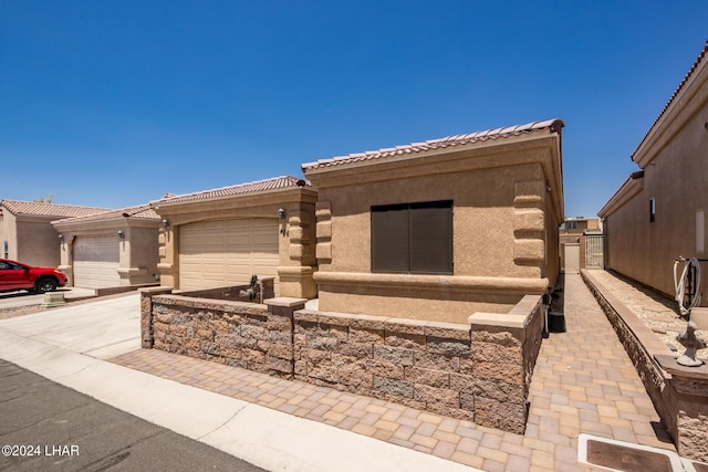 view of front facade with a tile roof, driveway, an attached garage, and stucco siding