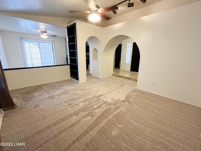 spare room featuring light carpet, ceiling fan, and arched walkways