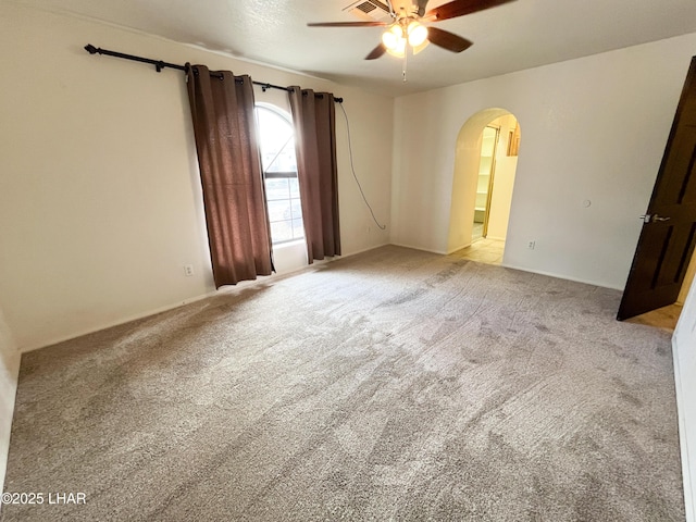 unfurnished room featuring a ceiling fan, arched walkways, and light carpet