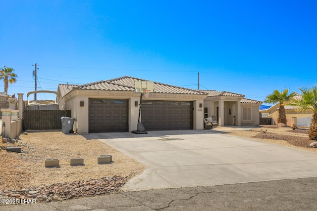 view of front of property featuring stucco siding, driveway, a tile roof, fence, and a garage