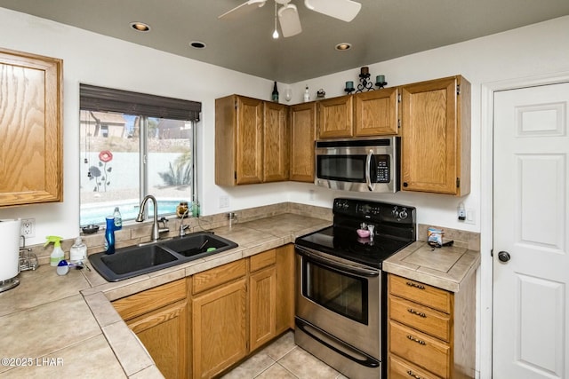 kitchen with appliances with stainless steel finishes, tile counters, brown cabinetry, and a sink