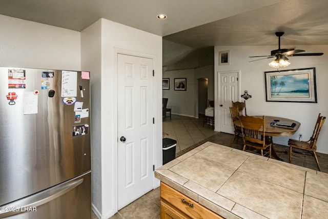 kitchen with arched walkways, tile countertops, freestanding refrigerator, vaulted ceiling, and tile patterned floors