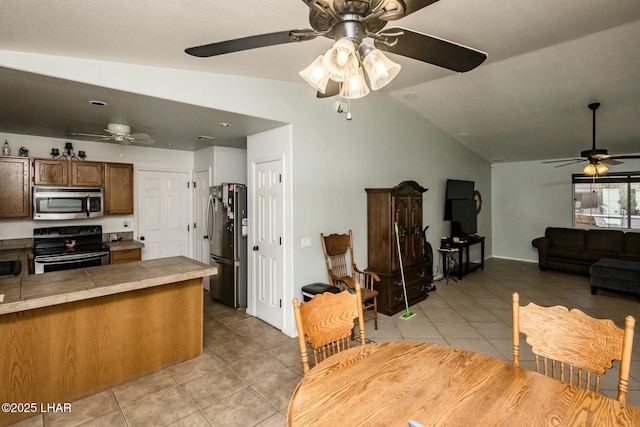 kitchen featuring brown cabinets, light tile patterned floors, tile counters, lofted ceiling, and appliances with stainless steel finishes