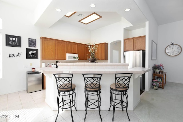 kitchen with tile countertops, stainless steel refrigerator, refrigerator, a kitchen bar, and light tile patterned floors