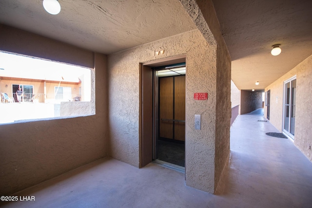 hallway featuring elevator, concrete floors, a textured ceiling, and a textured wall