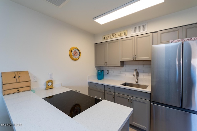 kitchen featuring tasteful backsplash, visible vents, freestanding refrigerator, gray cabinets, and a sink