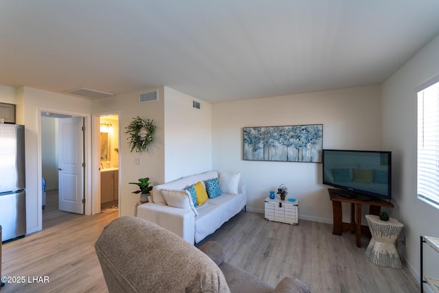 living room featuring light wood finished floors, visible vents, and baseboards