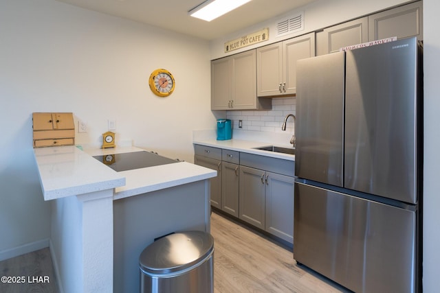 kitchen featuring a peninsula, a sink, backsplash, gray cabinets, and freestanding refrigerator