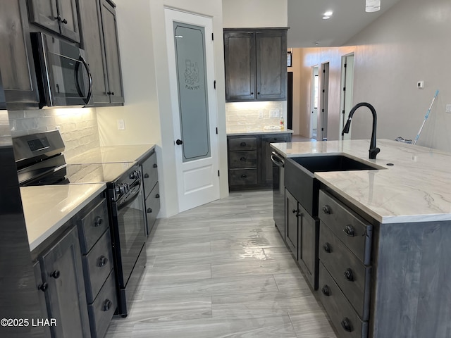 kitchen featuring a sink, light stone countertops, decorative backsplash, black appliances, and a kitchen island with sink