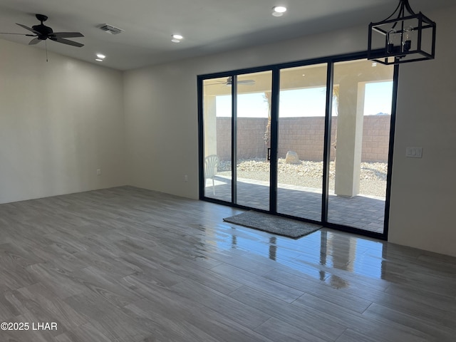 unfurnished room with visible vents, recessed lighting, ceiling fan with notable chandelier, and wood finished floors