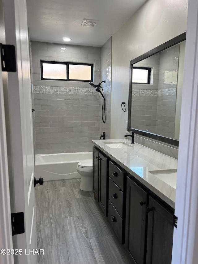 bathroom featuring visible vents, toilet, a sink, shower / washtub combination, and double vanity