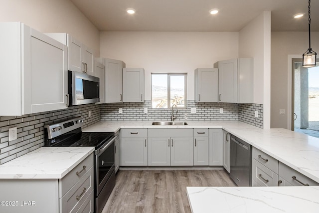 kitchen featuring stainless steel appliances, light stone countertops, light hardwood / wood-style floors, sink, and pendant lighting