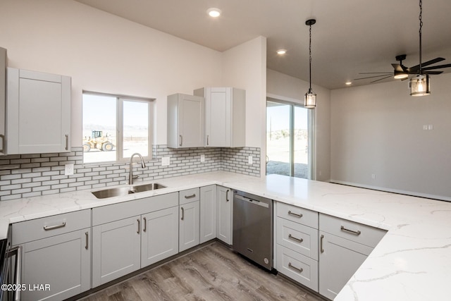 kitchen featuring light stone counters, stainless steel dishwasher, decorative light fixtures, backsplash, and sink