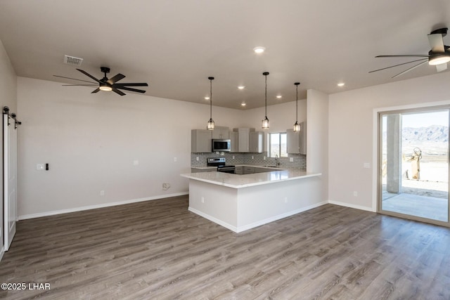 kitchen featuring appliances with stainless steel finishes, a barn door, kitchen peninsula, hanging light fixtures, and tasteful backsplash