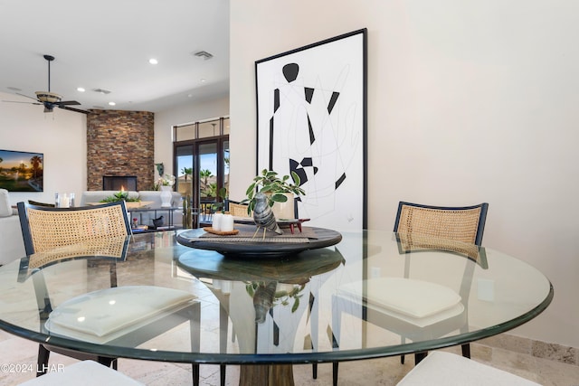 dining area with a stone fireplace and ceiling fan