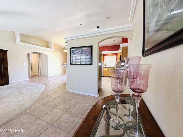 interior space with arched walkways, light tile patterned floors, vaulted ceiling, a sink, and baseboards