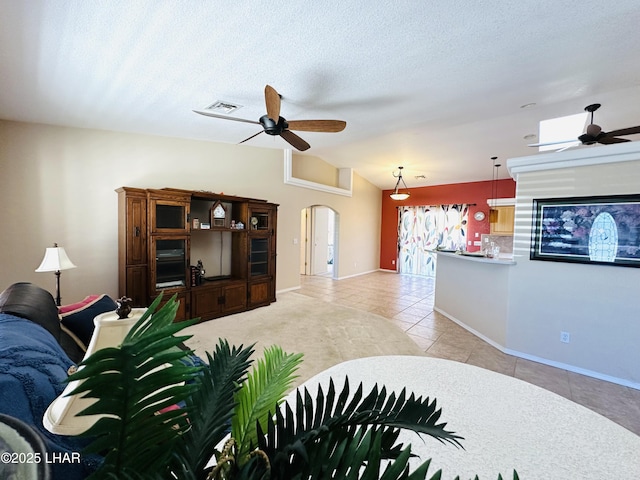 tiled living room with visible vents, arched walkways, vaulted ceiling, and a ceiling fan