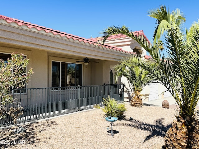 back of property with ceiling fan, a tile roof, and stucco siding