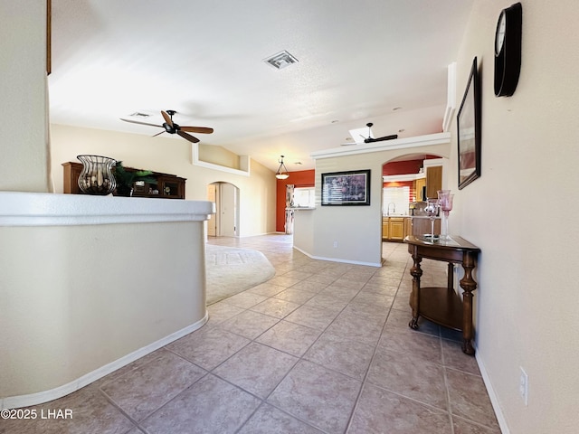 hallway featuring arched walkways, light tile patterned floors, visible vents, baseboards, and vaulted ceiling