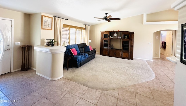 carpeted living area featuring arched walkways, lofted ceiling, a ceiling fan, tile patterned flooring, and baseboards