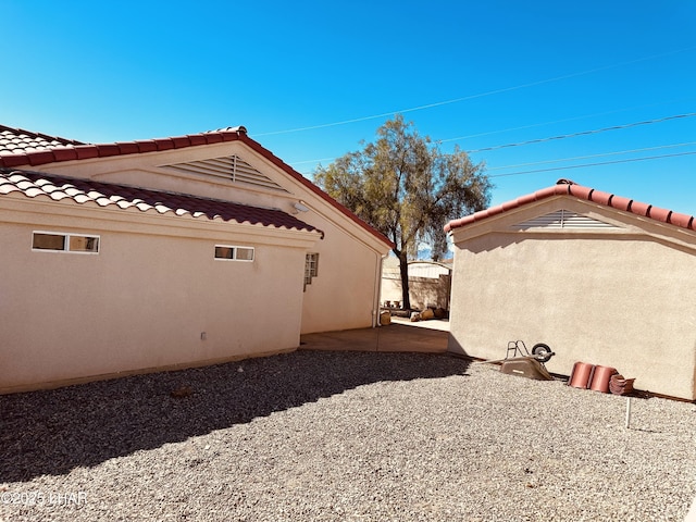 view of side of home featuring a tiled roof, a patio, and stucco siding