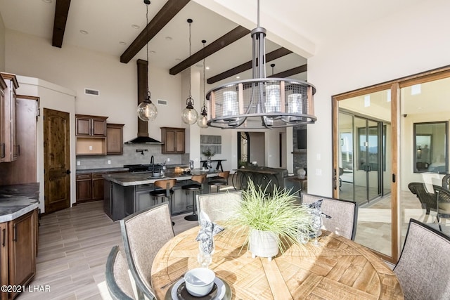 dining room with a towering ceiling, beamed ceiling, sink, light hardwood / wood-style floors, and an inviting chandelier