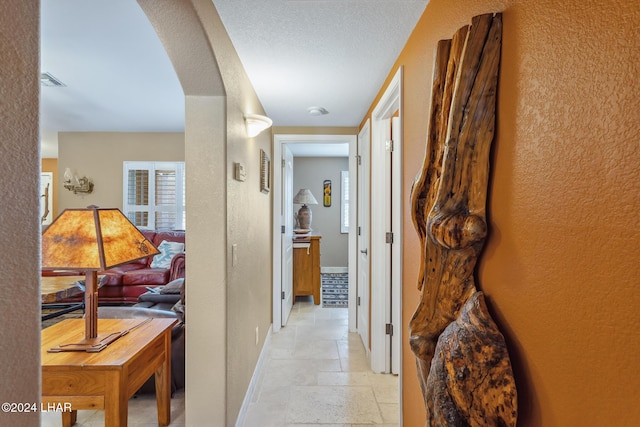 corridor with baseboards, arched walkways, stone tile floors, and a textured wall