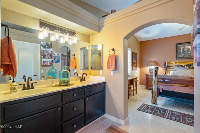 ensuite bathroom featuring double vanity, connected bathroom, baseboards, and a sink