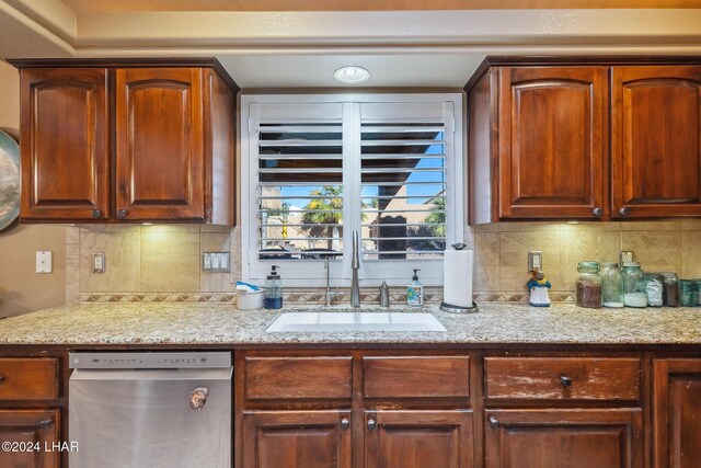 kitchen featuring stainless steel dishwasher, decorative backsplash, light stone countertops, and a sink