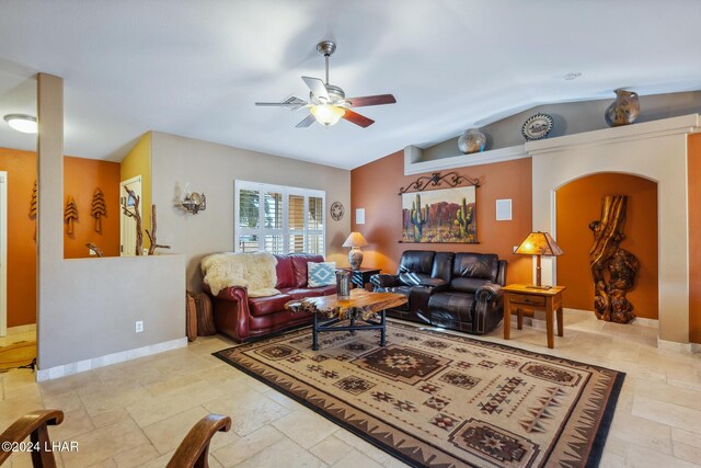 living area with ceiling fan, vaulted ceiling, baseboards, and stone tile flooring