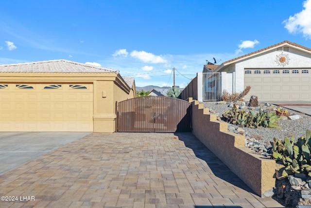 view of side of home featuring stucco siding, a tiled roof, driveway, and a gate