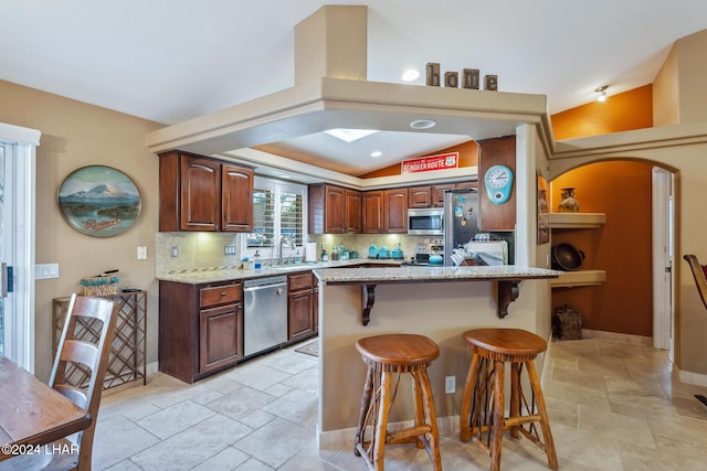 kitchen with stone tile flooring, a breakfast bar area, backsplash, and stainless steel appliances