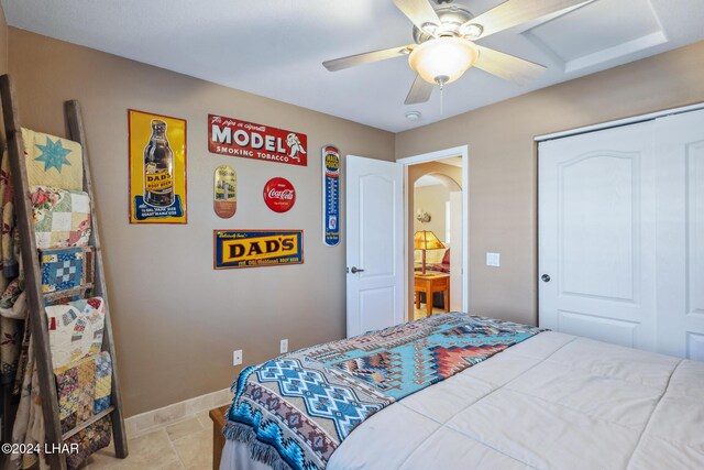 bedroom featuring a closet, arched walkways, light tile patterned floors, baseboards, and ceiling fan