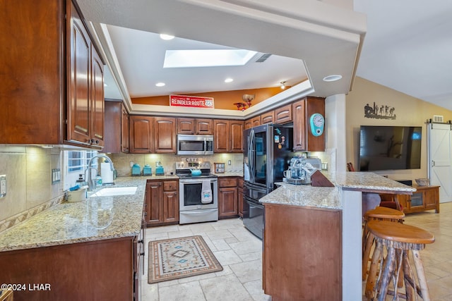 kitchen with a peninsula, vaulted ceiling with skylight, a sink, decorative backsplash, and stainless steel appliances