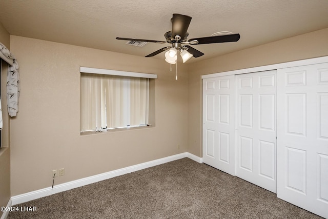 unfurnished bedroom with dark colored carpet, ceiling fan, a textured ceiling, and a closet