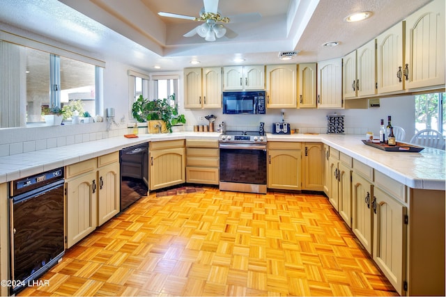 kitchen featuring black appliances, light parquet floors, ceiling fan, kitchen peninsula, and a raised ceiling