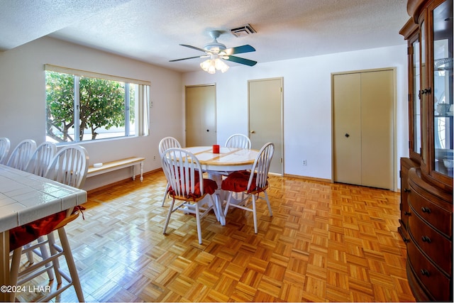 dining area with ceiling fan, light parquet flooring, and a textured ceiling