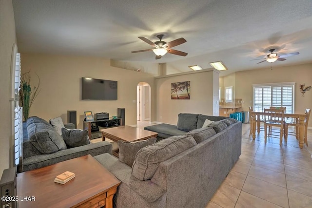 living room with light tile patterned floors, arched walkways, vaulted ceiling, and a ceiling fan