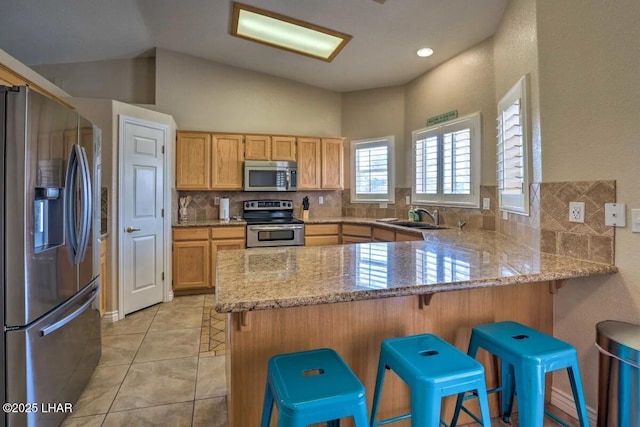 kitchen with a peninsula, a sink, light stone countertops, stainless steel appliances, and backsplash