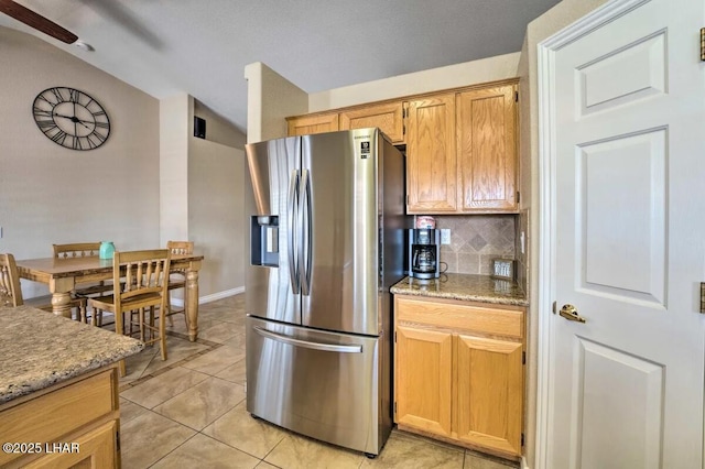 kitchen featuring light tile patterned floors, tasteful backsplash, lofted ceiling, light stone countertops, and stainless steel fridge