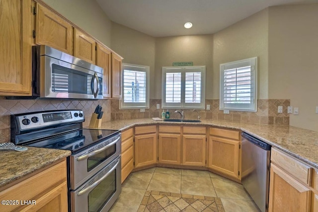 kitchen featuring light tile patterned floors, a sink, appliances with stainless steel finishes, backsplash, and light stone countertops