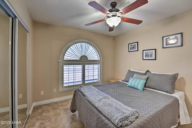 bedroom featuring a closet, a ceiling fan, a textured ceiling, tile patterned flooring, and baseboards