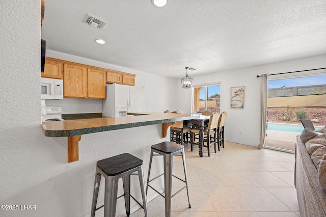 kitchen featuring a peninsula, white appliances, visible vents, dark countertops, and a kitchen bar