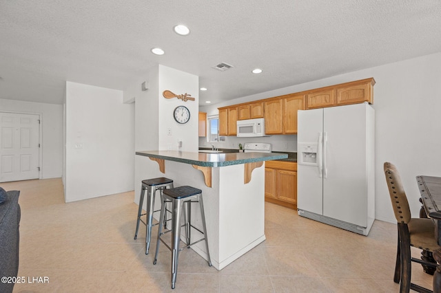 kitchen featuring a breakfast bar area, a peninsula, white appliances, visible vents, and dark countertops