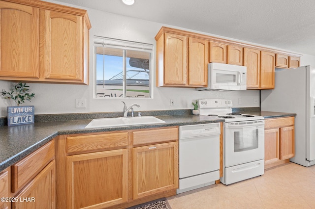 kitchen with light tile patterned floors, dark countertops, a sink, a textured ceiling, and white appliances