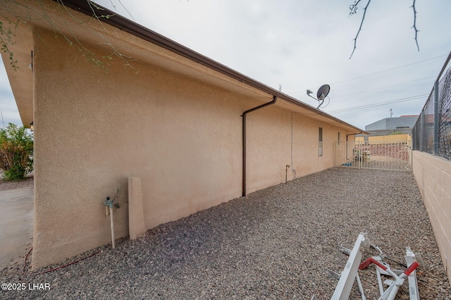 view of side of property with a gate, fence, and stucco siding